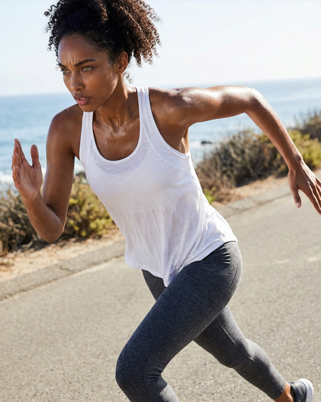 Woman running outdoors in a white athletic tank top and gray leggings by the ocean