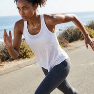 Woman running outdoors in a white athletic tank top and gray leggings by the ocean