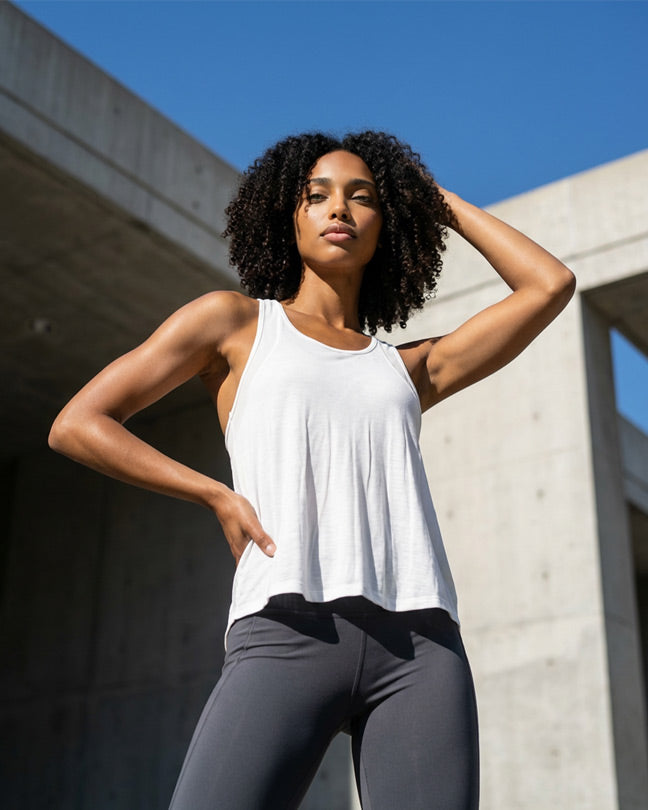 Woman wearing white tank top and gray leggings posing outdoors in sunlight