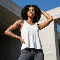 Woman wearing white tank top and gray leggings posing outdoors in sunlight