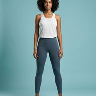 Woman in white sleeveless athletic top and gray leggings standing against a blue background