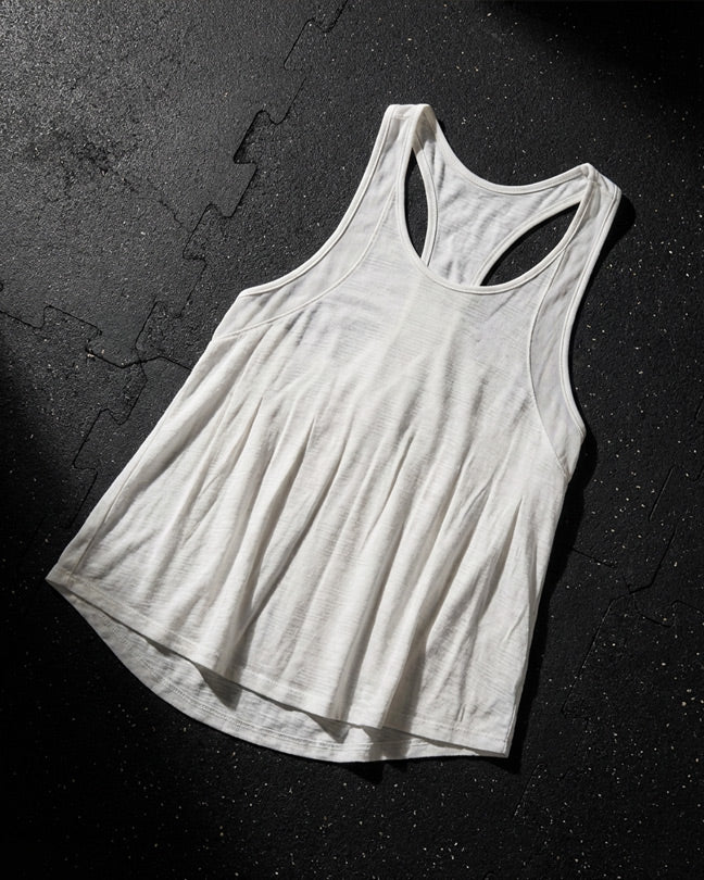 White racerback tank top with lightweight fabric on a textured black gym floor