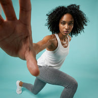 Woman in athletic white tank top and gray leggings posing in active lunge on blue background