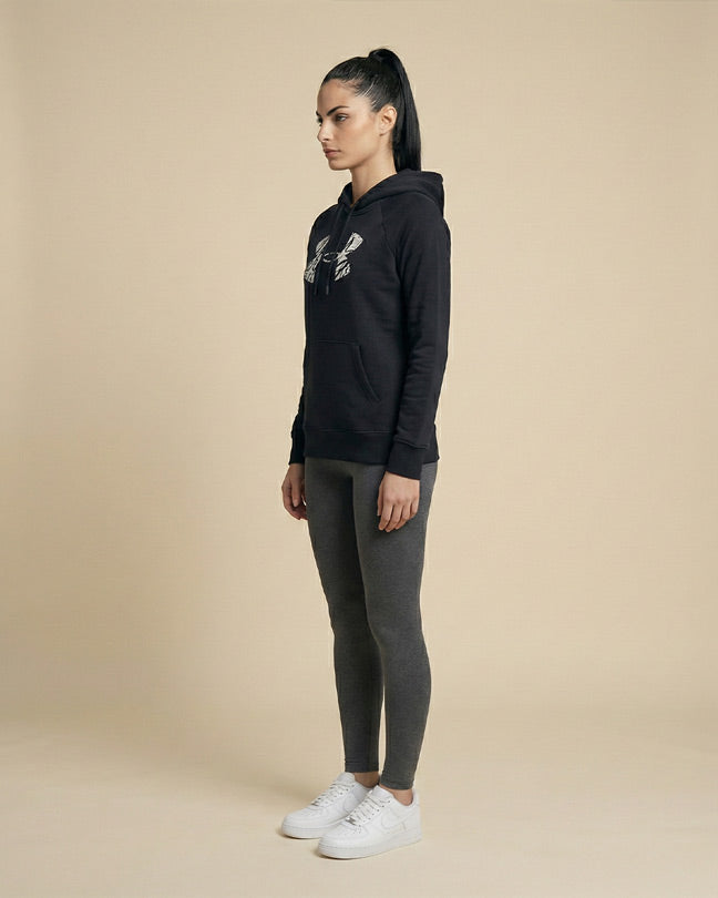 Woman wearing black graphic hoodie, grey leggings, and white sneakers standing in studio
