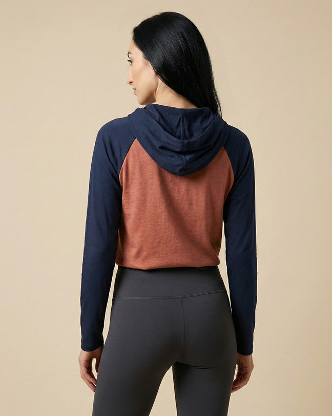 Woman wearing two-tone hooded long sleeve top and black leggings, shown from the back