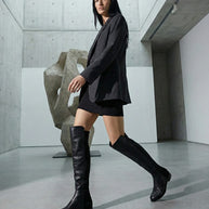 Woman in black blazer and mini skirt wearing tall black boots in a modern gallery setting