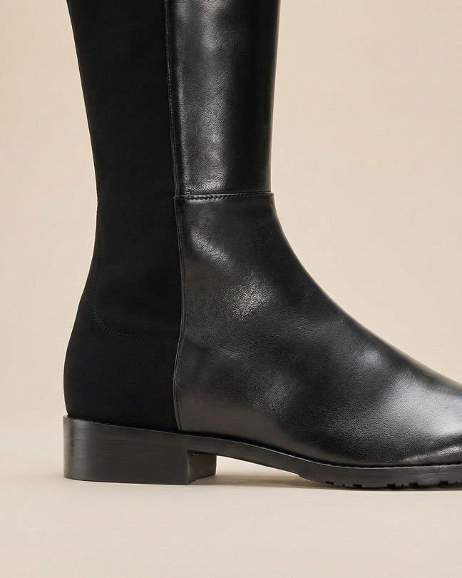 Black leather knee-high boot with low heel and side panel on neutral background
