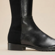 Black leather knee-high boot with low heel and side panel on neutral background