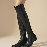 Women's black knee-high leather boots on beige background