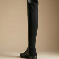 Black knee-high leather boot with flat heel on neutral background