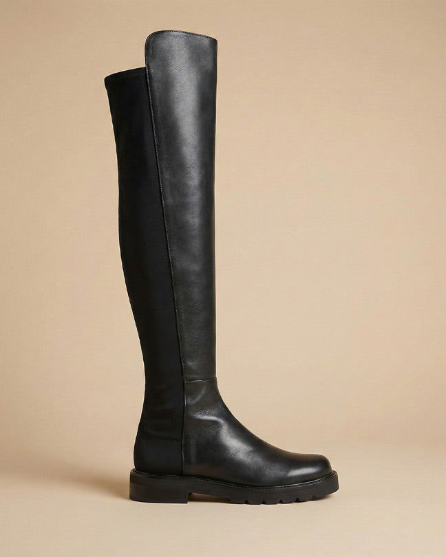 Black knee-high leather boot with a chunky sole on a neutral background