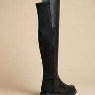 Black over-the-knee boot with flat sole, leather and suede design, side profile on beige background