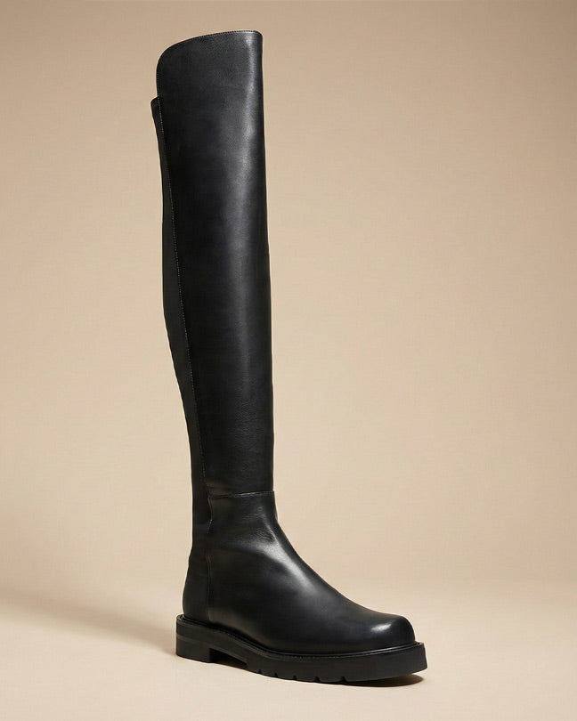 Black over-the-knee leather boot with chunky sole on beige background
