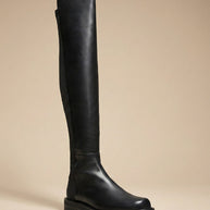 Black over-the-knee leather boot with chunky sole on beige background