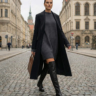 Woman in black coat, grey sweater dress and knee-high boots walking on city street