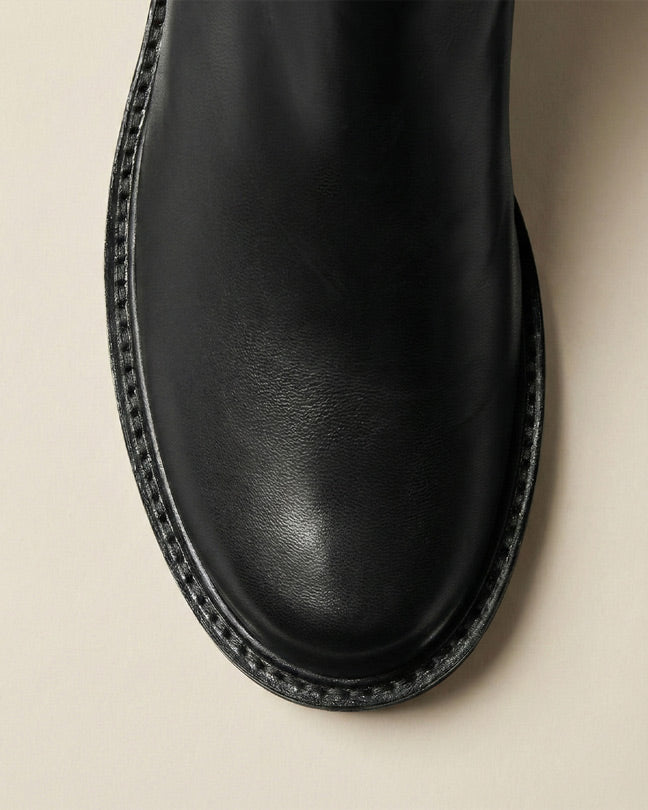 Close-up of black leather boot toe with detailed stitching on a neutral background