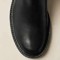 Close-up of black leather boot toe with detailed stitching on a neutral background