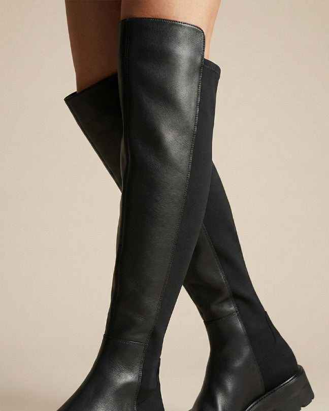 Black over-the-knee boots with leather and fabric panels on a neutral background