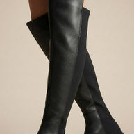 Black over-the-knee boots with leather and fabric panels on a neutral background