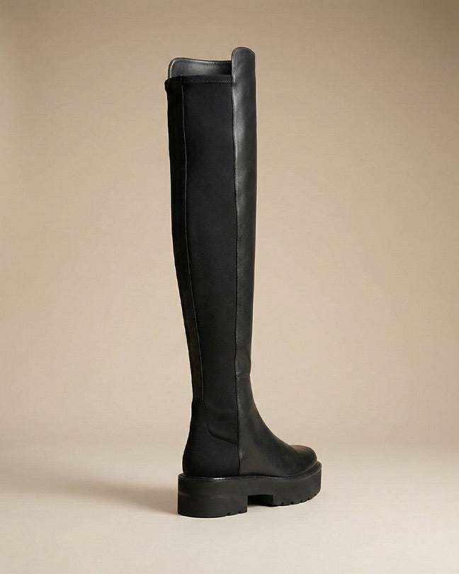 Black over-the-knee boot with chunky sole on neutral background