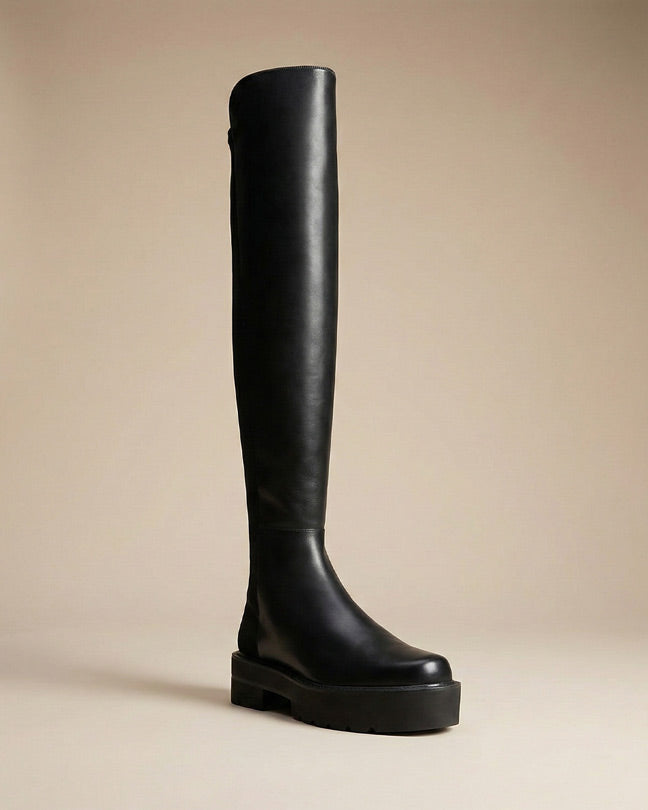 Black over-the-knee platform boot with thick sole on neutral background