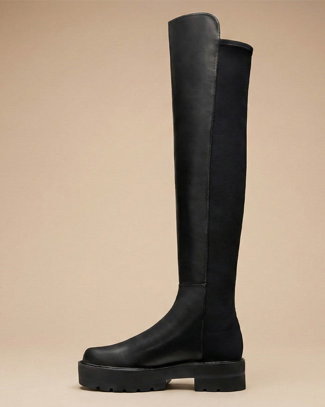 Black over-the-knee riding boot with chunky sole on neutral background