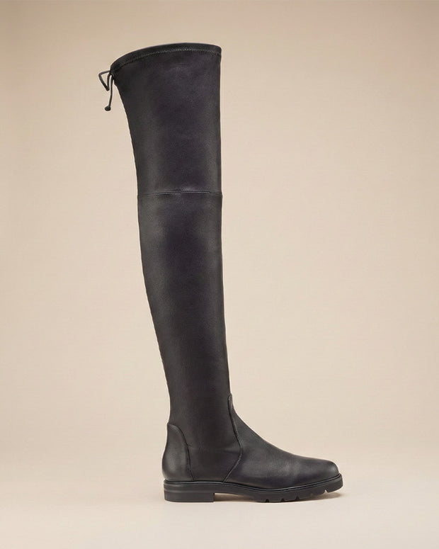 Black over the knee boot with flat sole and side tie detail on beige background