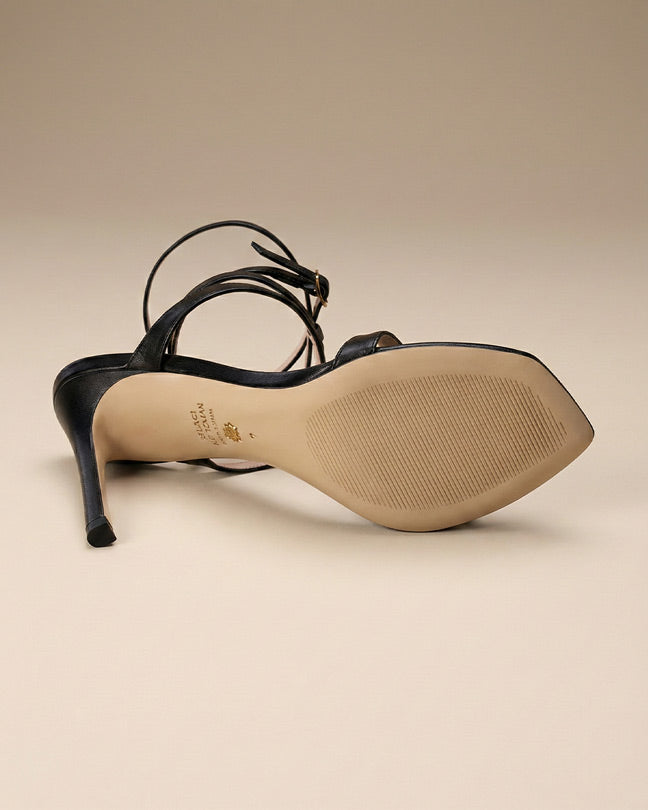Black high heel sandal with ankle strap, viewed from sole on neutral background