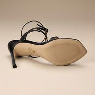 Black high heel sandal with ankle strap, viewed from sole on neutral background