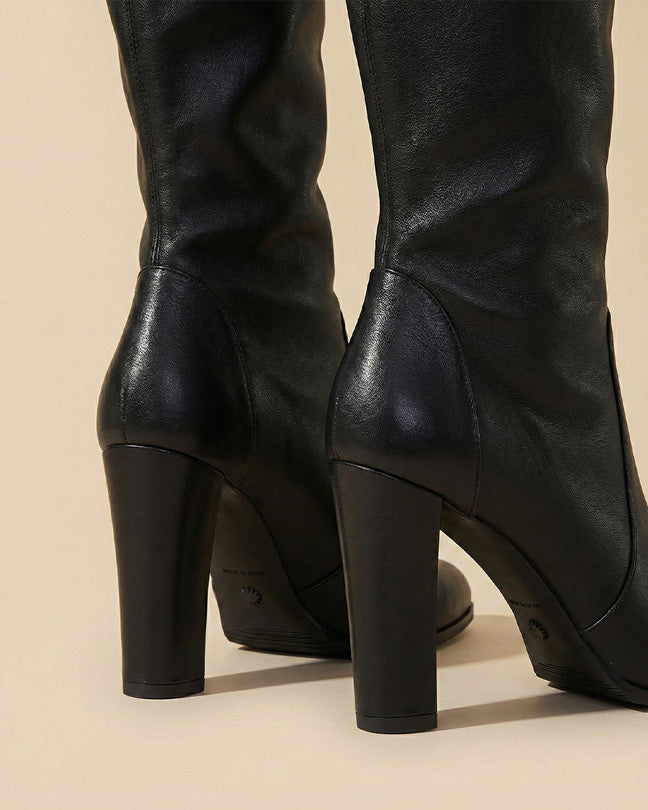 Close-up of black leather knee-high boots with block heels on beige background