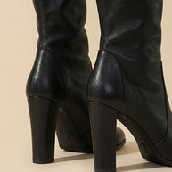 Close-up of black leather knee-high boots with block heels on beige background