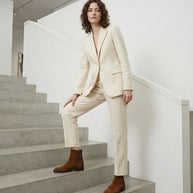Woman in a cream suit and brown boots posing on modern concrete stairs indoors
