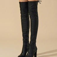 Black over-the-knee heeled boots with drawstring back detail on beige background