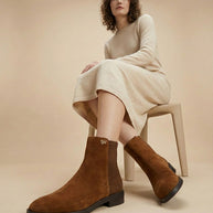 Woman in beige sweater dress modeling brown suede ankle boots on neutral background
