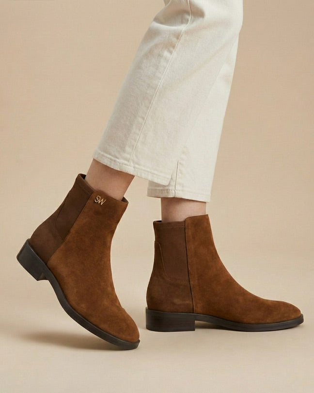 Brown suede ankle boots worn with cream cropped pants on beige background
