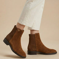 Brown suede ankle boots worn with cream cropped pants on beige background