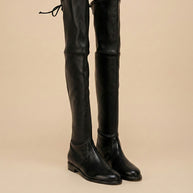 Black over the knee leather boots with low heel and tie detail, neutral background