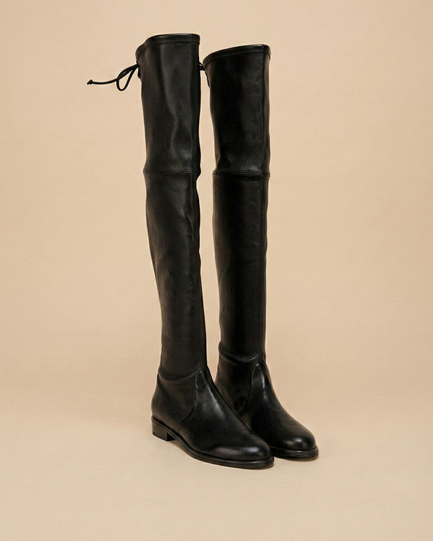 Black over the knee leather boots with low heel and tie detail, neutral background