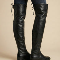 Black over-the-knee leather boots with low heels and lace-up back details, worn with jeans