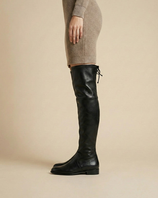 Woman wearing black over-the-knee leather boots and a beige knit dress, side view