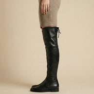 Woman wearing black over-the-knee leather boots and a beige knit dress, side view