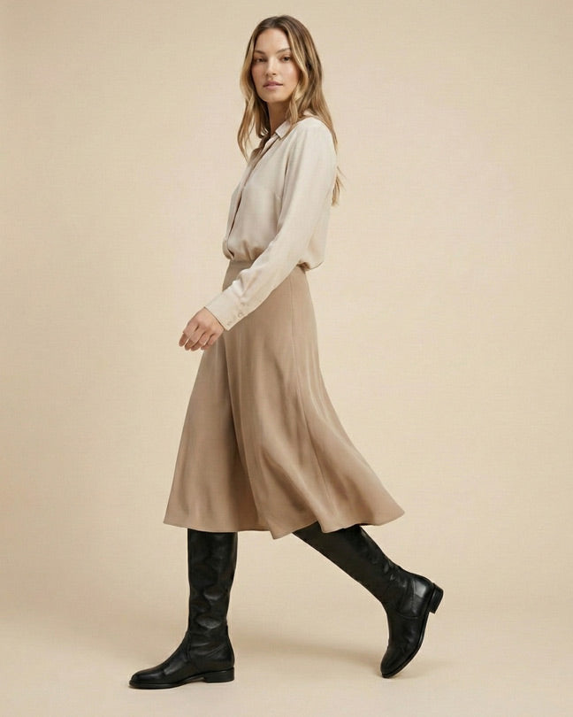 Woman wearing beige blouse, tan midi skirt, and black knee-high boots, side view