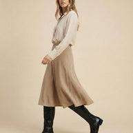 Woman wearing beige blouse, tan midi skirt, and black knee-high boots, side view