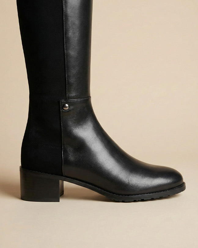 Black knee-high leather boot with block heel on beige background