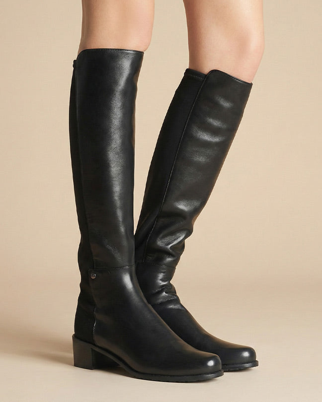 Black knee-high leather boots with low block heels on model against neutral background