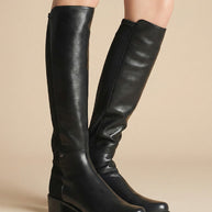 Black knee-high leather boots with low block heels on model against neutral background