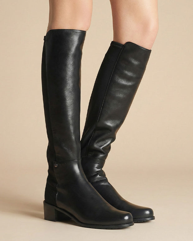 Black knee-high leather boots with low block heels on model against neutral background