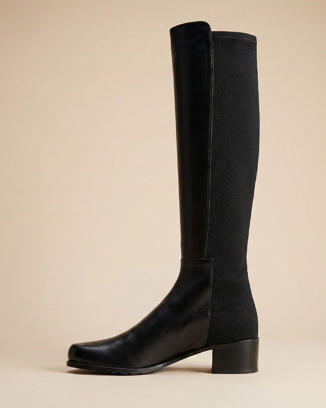 Black knee-high boot with block heel on beige background, side view