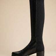 Black knee-high boot with block heel on beige background, side view