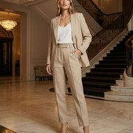 Woman in beige pantsuit and white top standing in elegant marble lobby with chandelier